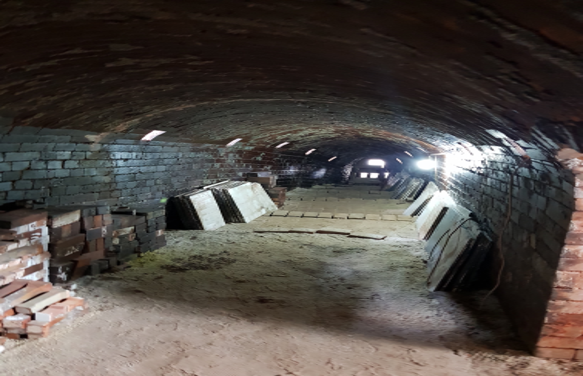 A dim brick tunnel with an arched ceiling, stacked bricks along the walls, and light at the far end.